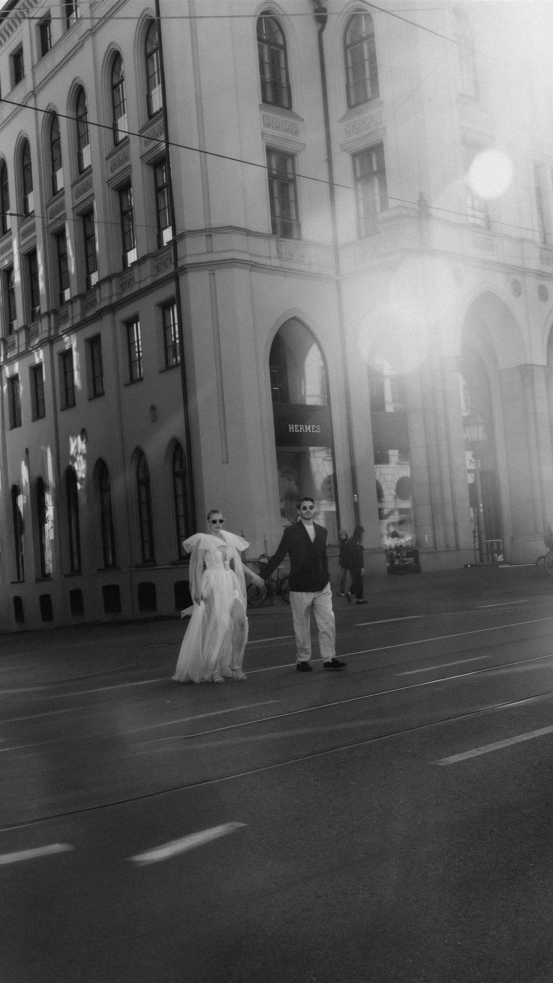 Couple crossing a Munich tram boulevard, black and white with sun flare
