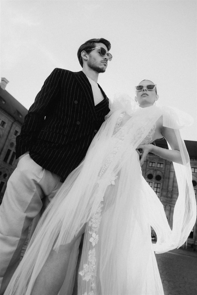 Low-angle portrait of a couple in wedding attire in front of the Residenz facade, Munich.