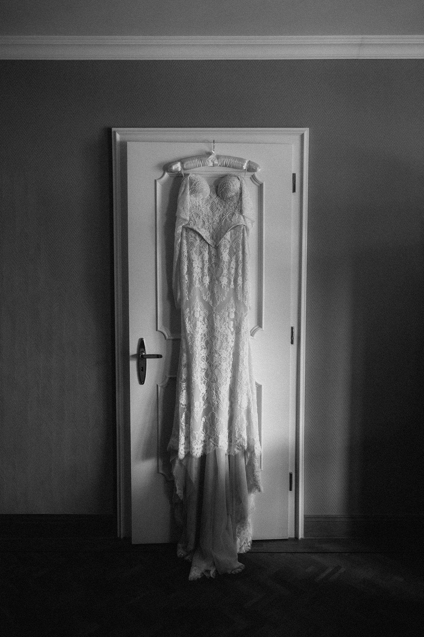 Sophia’s lace wedding dress hangs on a door in black and white.