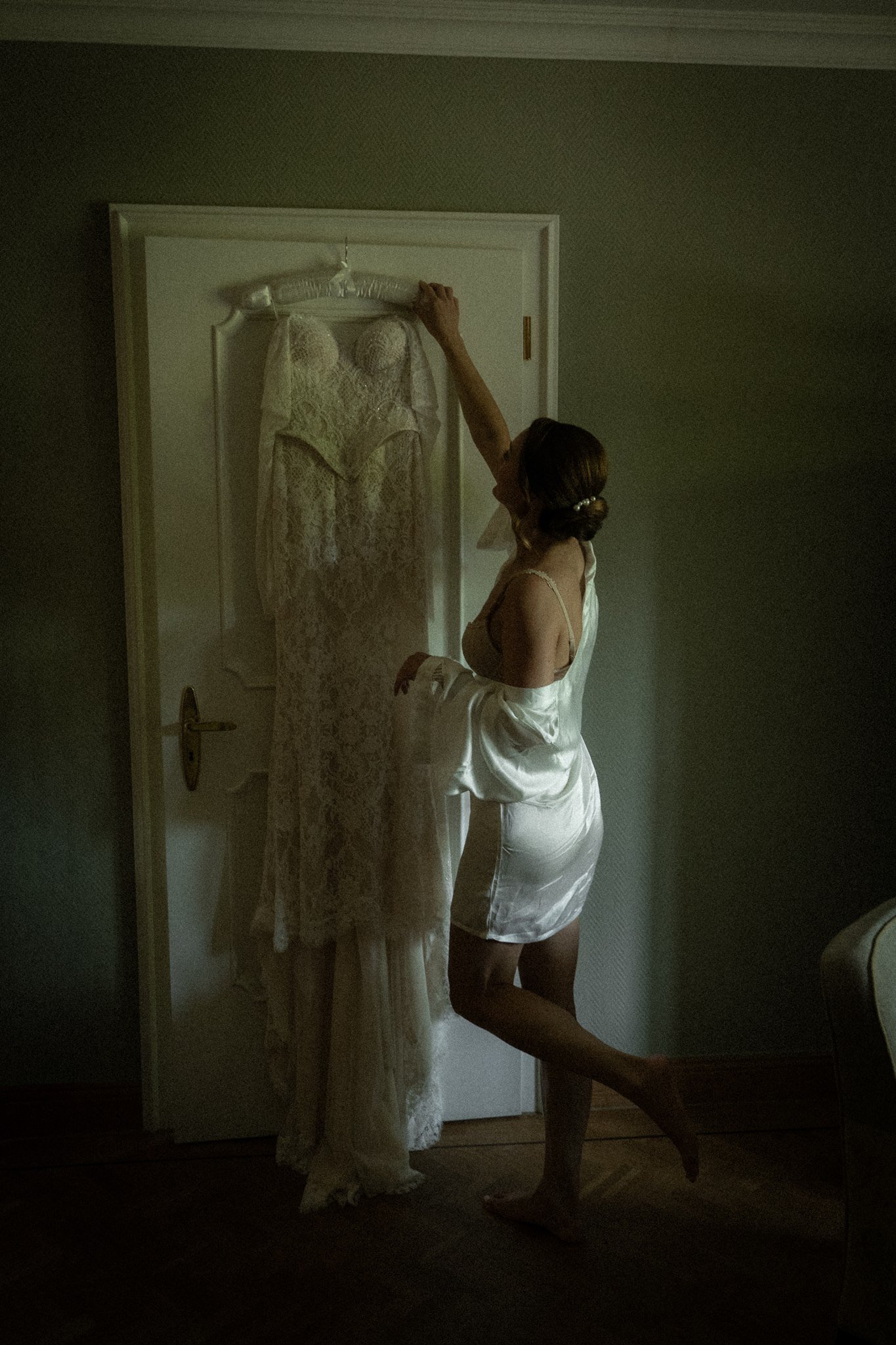 Sophia in a silk robe reaches for her lace wedding dress.