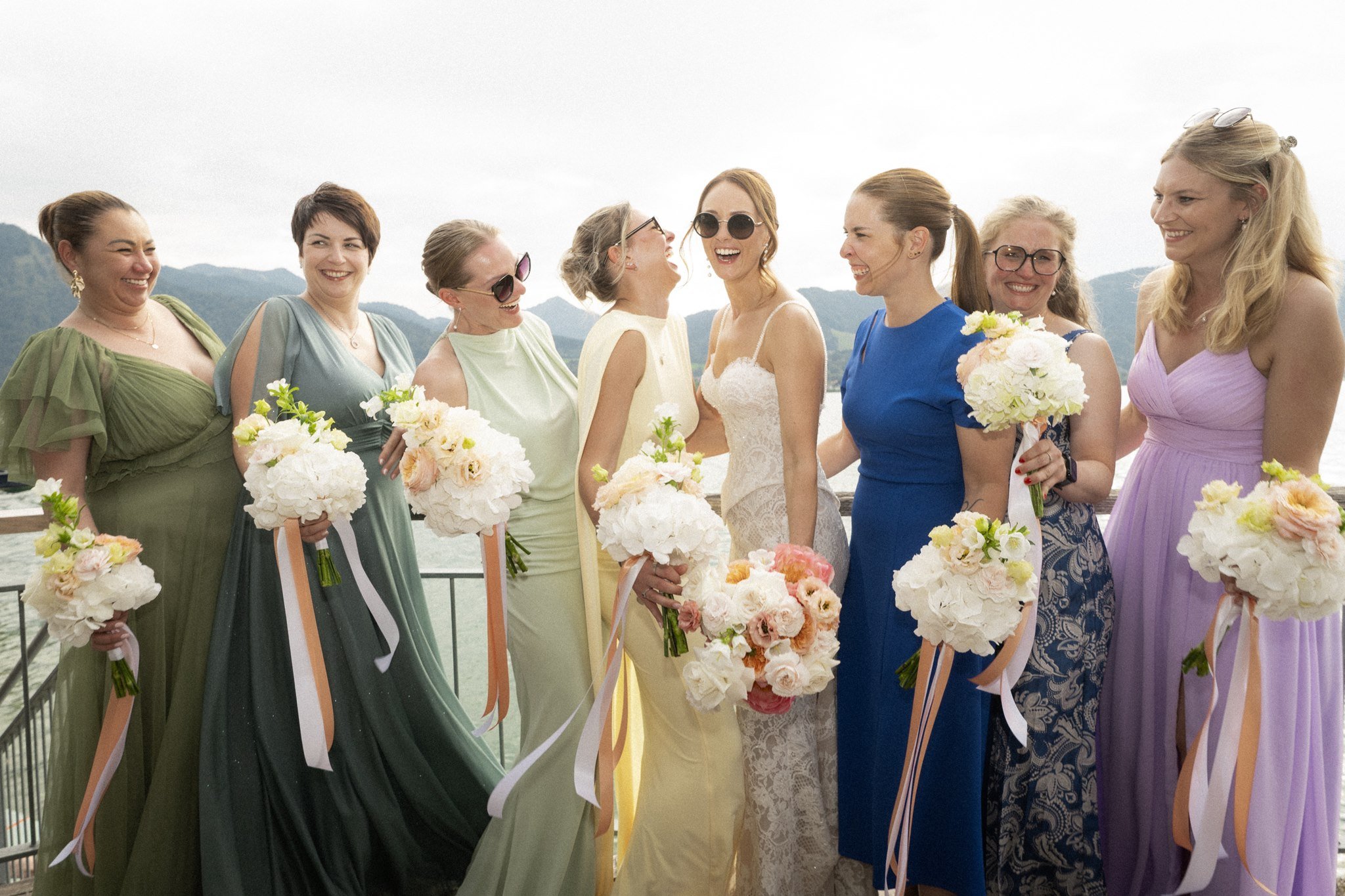 Sophia laughs with her bridesmaids in pastel dresses by Lake Tegernsee.