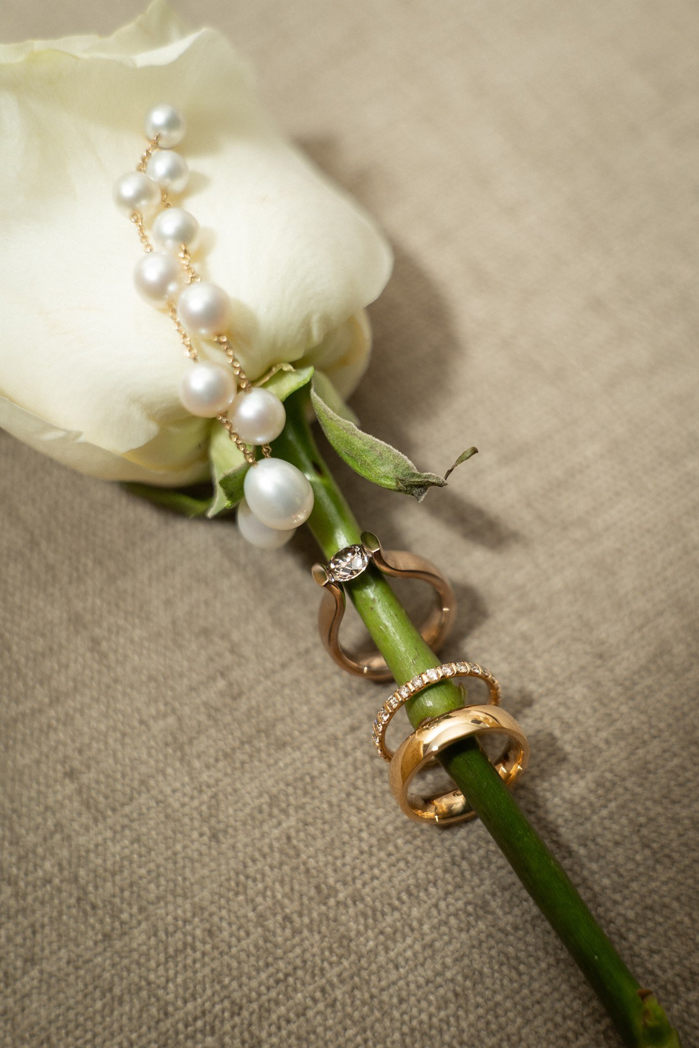 A white rose with a pearl earring and gold wedding rings.