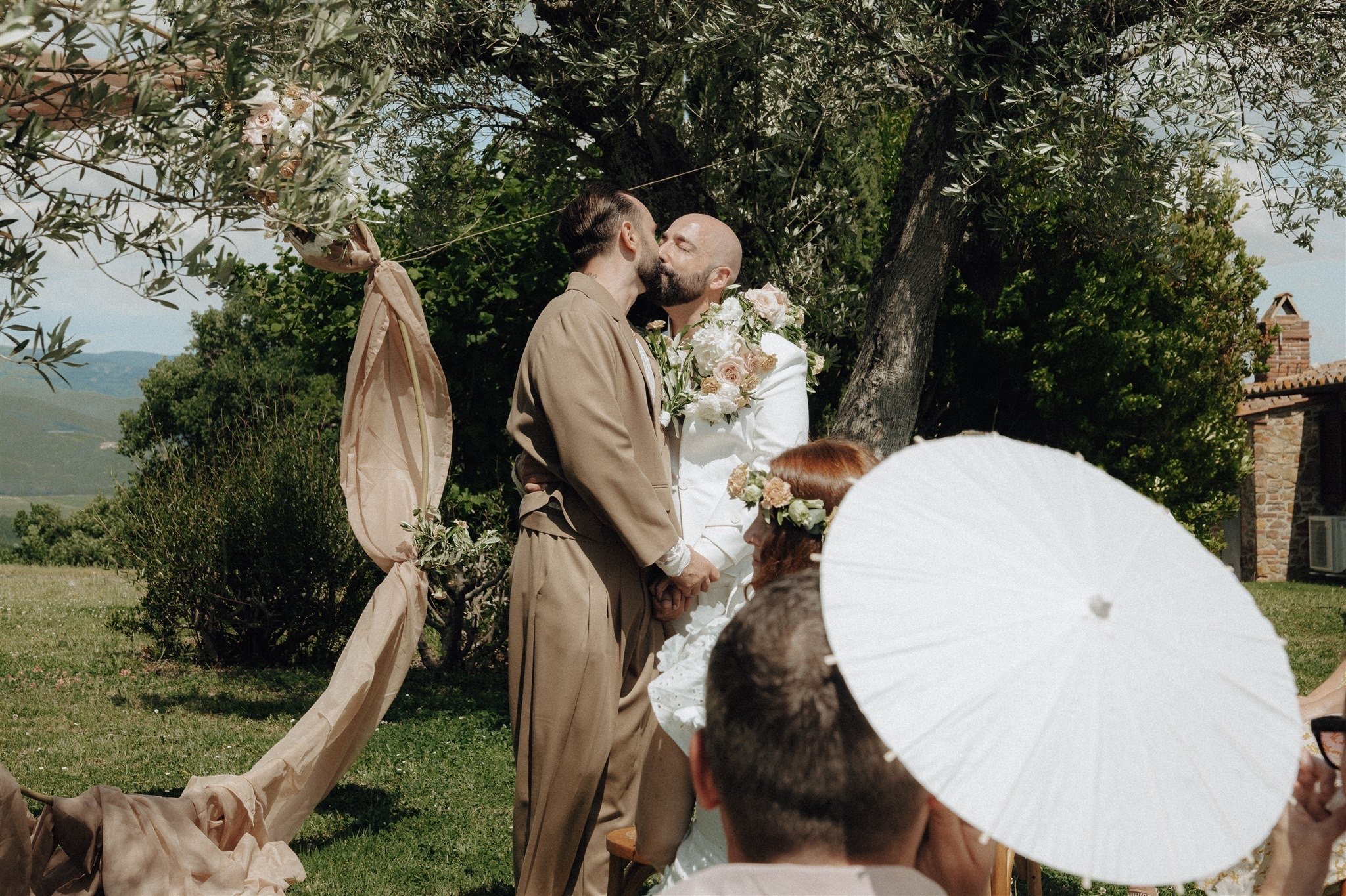 Tony and Patryk kiss during an outdoor ceremony among olive trees in Tuscany.