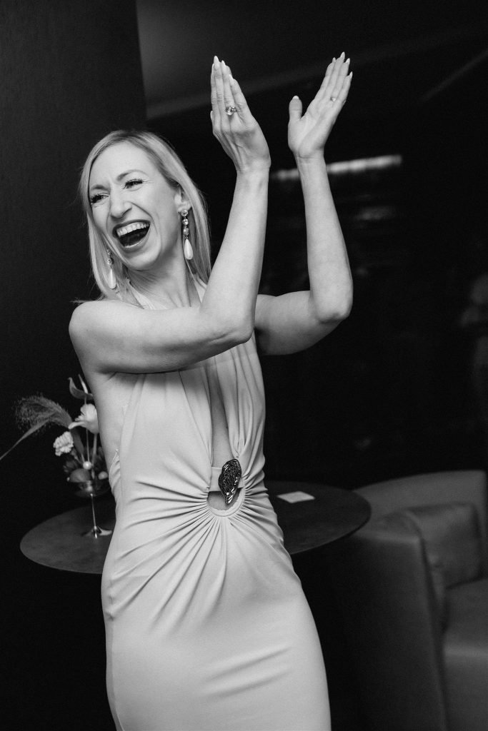 Guest in a draped dress laughing during a wedding celebration in Munich, black and white.