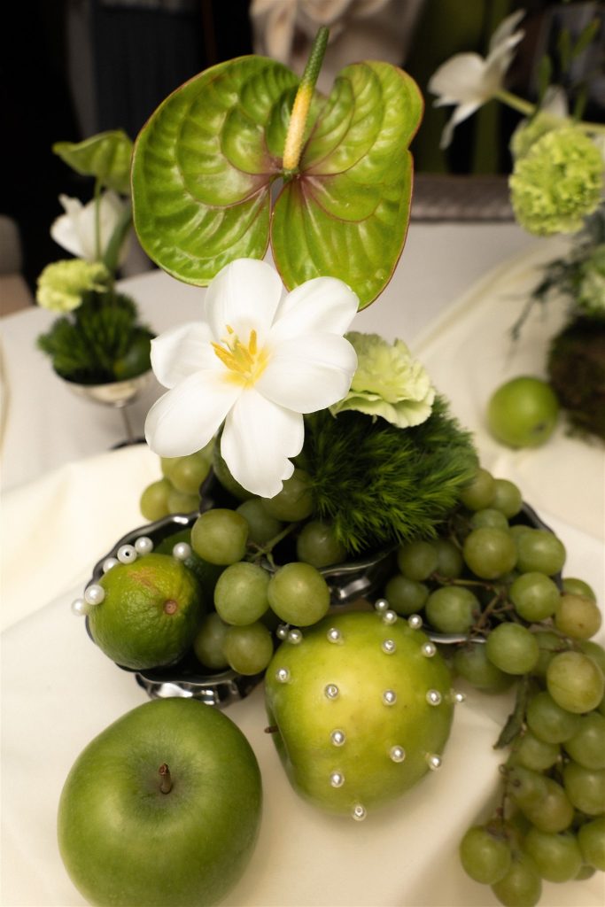 Green centerpiece with anthurium, white tulip, grapes and a pearl-pinned apple.