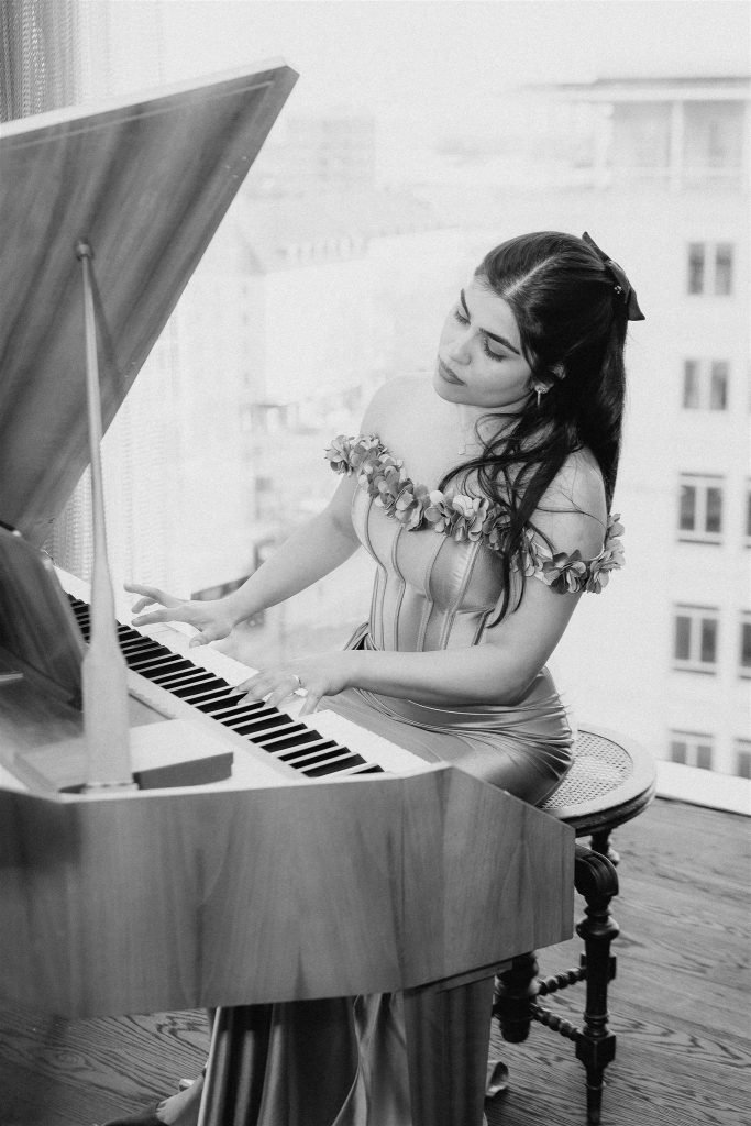 Pianist in a gold gown at a grand piano by the window with the skyline of Munich, black and white.