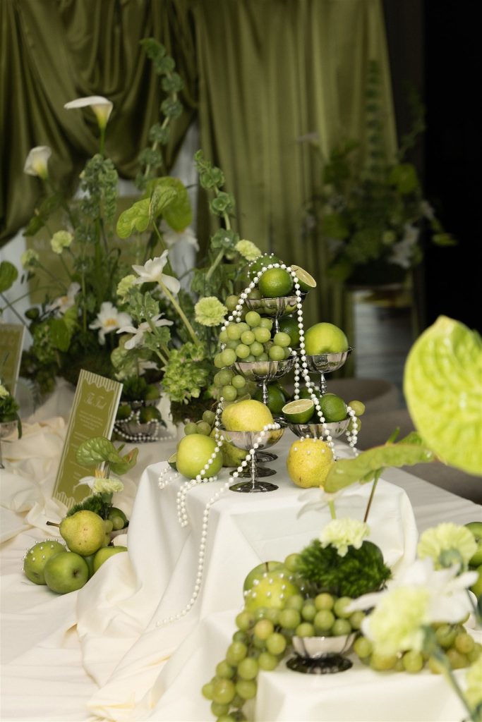 Wedding table styled in green and cream with a silver coupe of fruit, grapes and pearl details.