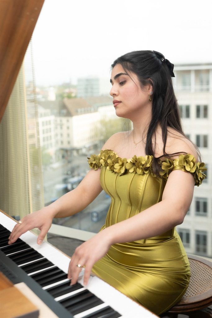 Pianist in a golden dress at the piano in front of a window with a view over Munich.