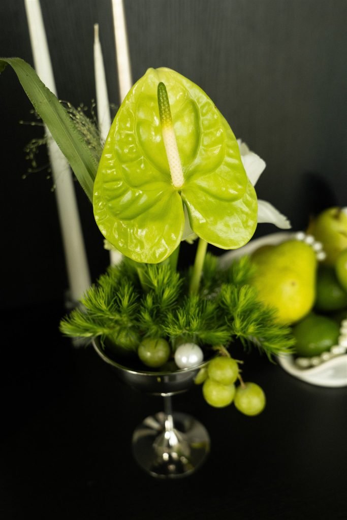 Green anthurium flower, pears and candles on a dark table with pearl details.
