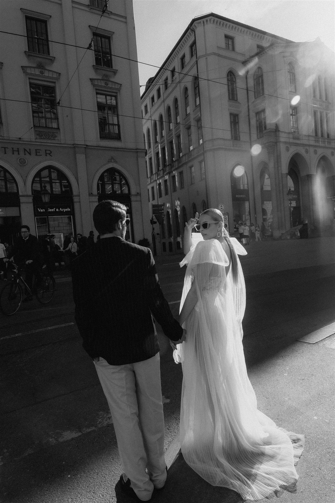 Couple in wedding attire crossing a Munich street in the sun, black and white.