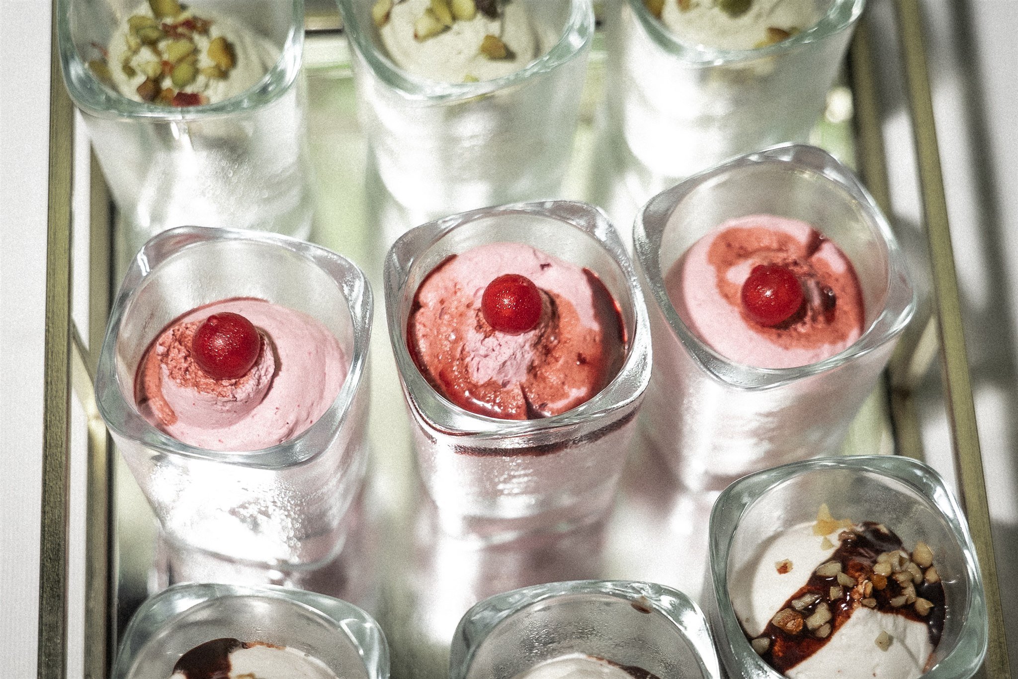 Dessert glasses with cherry and pistachio creams on a mirrored tray