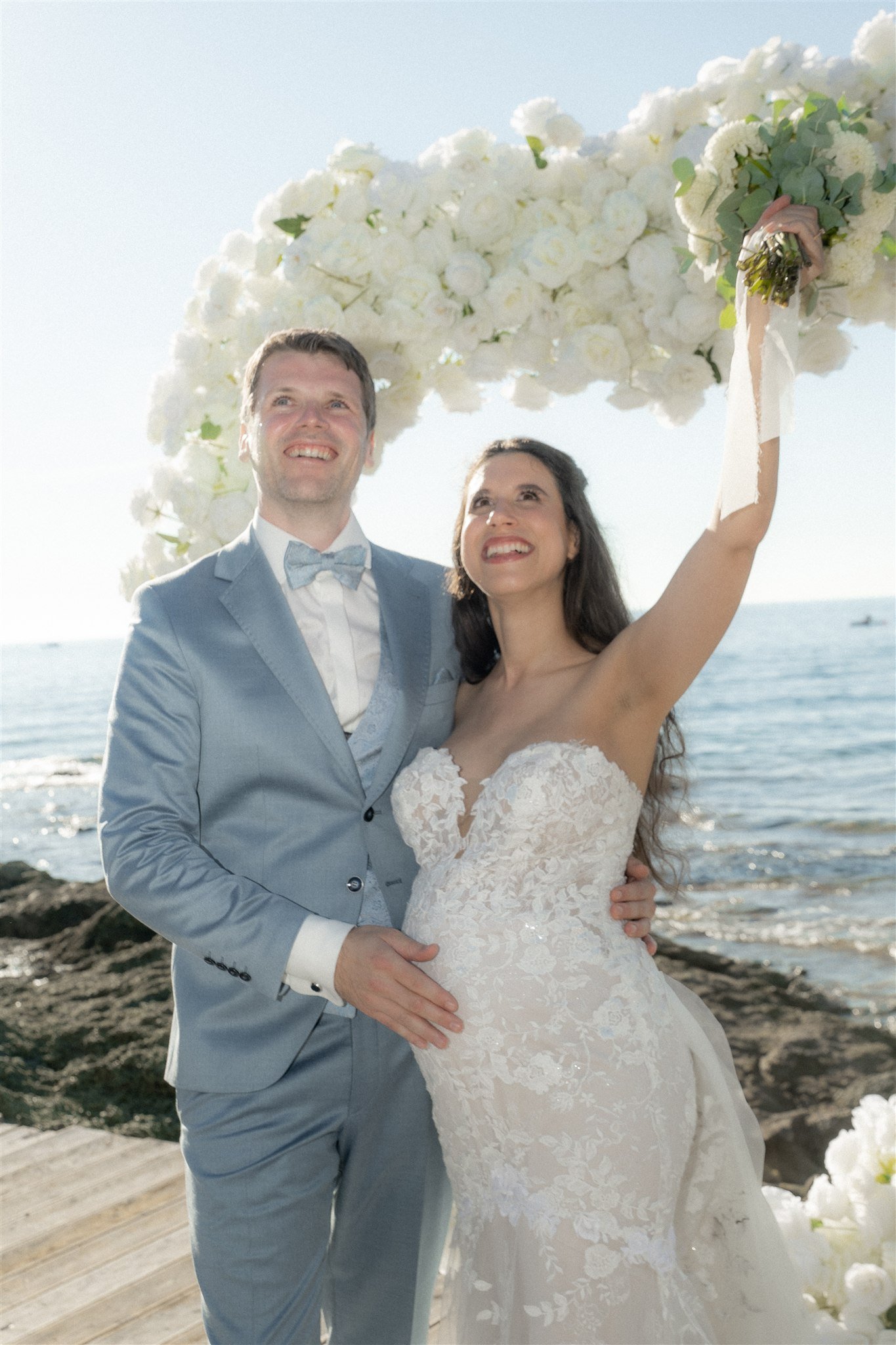 Newlyweds under the white floral arch by the sea