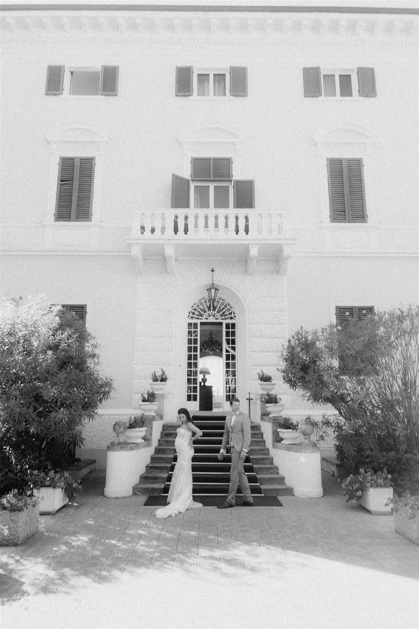 The white facade of Grand Hotel Villa Parisi, newlyweds on the entrance steps in black and white
