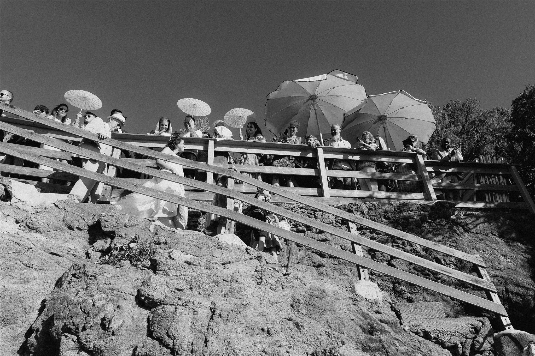 Bride descending the wooden staircase to the beach with guests above
